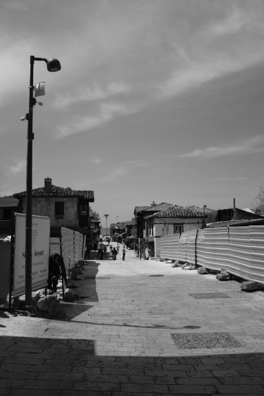 Strada stretta con edifici ai lati e cielo nuvoloso in bianco e nero.